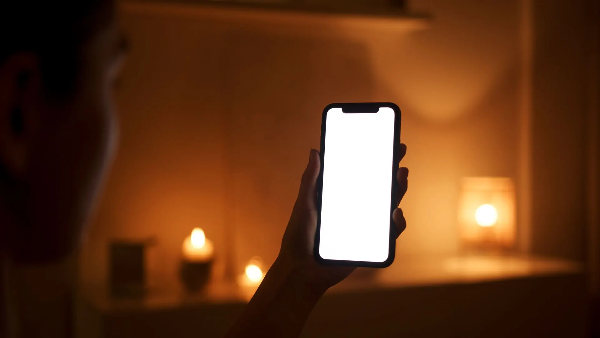 A person checking a glowing phone in a dark, candlelit room at night