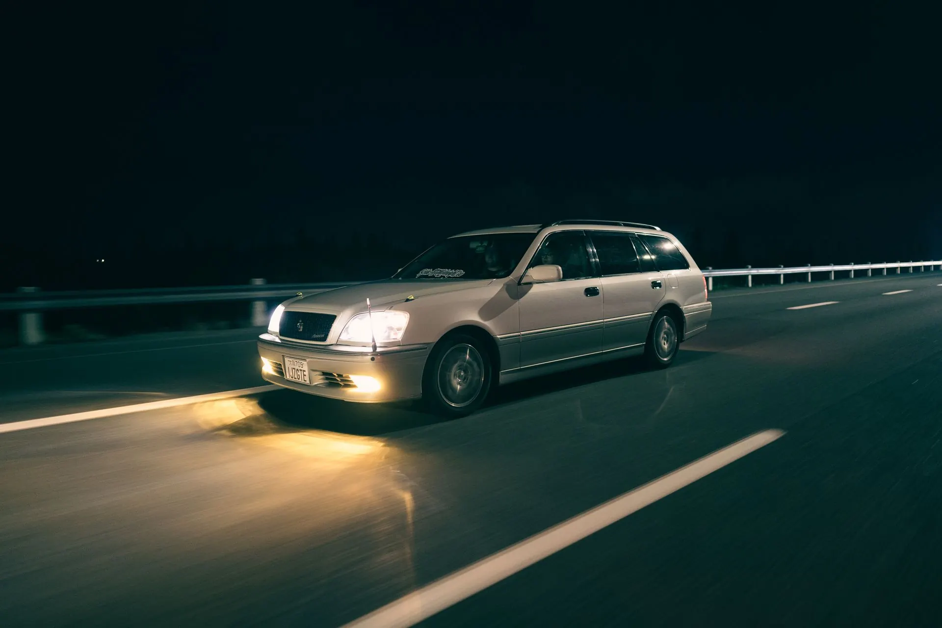 A car on a dark highway at night, headlights lighting the road